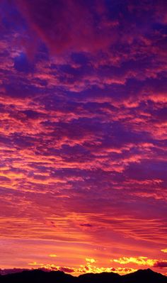 an airplane is flying in the sky at sunset with clouds and mountains behind it as the sun sets