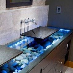 a bathroom with two sinks and blue rocks in the water under them, along with a faucet