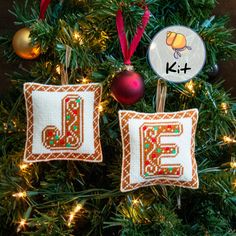 two cross stitch christmas ornaments hanging from a tree with the letter e on it's side