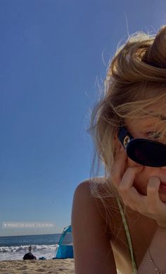 a woman on the beach with her sunglasses up to her face