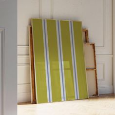 an empty room with a green and white striped painting on the wall next to a wooden shelf