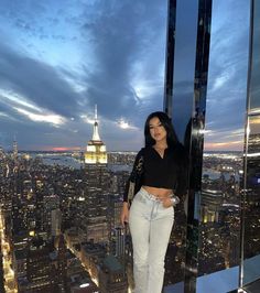 a woman standing on top of a tall building in the middle of a city at night