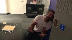 a man sitting on the floor in front of a locker with his hand up and thumbs up