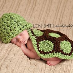 a baby wearing a green and brown crocheted hat with a turtle on it