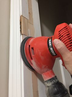 a hand holding a red blow dryer on top of a white door knobs