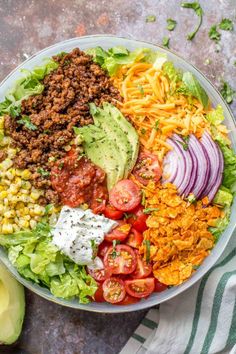 a bowl filled with taco salad next to an avocado and sliced tomatoes