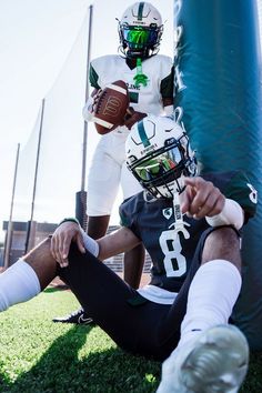 two football players sitting on the ground with one holding a ball in his right hand