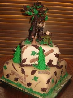 a three tiered cake decorated with trees and animals on it's sides, sitting on top of a wooden table