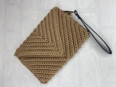 a brown knitted pouch sitting on top of a white bed next to a black strap