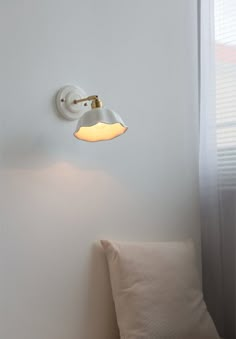 a white wall light mounted on the side of a wall next to a pillow and window