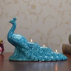 a blue peacock candle holder sitting on top of a table next to books and flowers