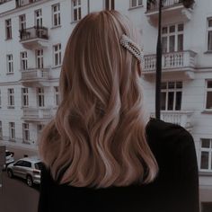 a woman with long blonde hair standing in front of a building and looking at the street