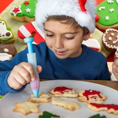 a young boy decorating christmas cookies with icing and decorations on the table in front of him