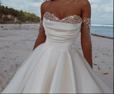 a woman is standing on the beach wearing a white wedding dress with sequins