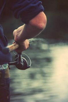 a man holding a fishing rod while standing next to a body of water