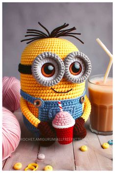 a crocheted minion holding a cupcake next to a glass of milk