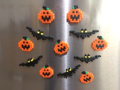 six perler beads arranged in the shape of pumpkins on a metal surface,