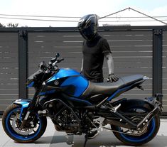 a man wearing a helmet standing next to a blue and black motorbike in front of a fence