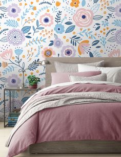 a bedroom with floral wallpaper and bedding in pink, blue, orange and white