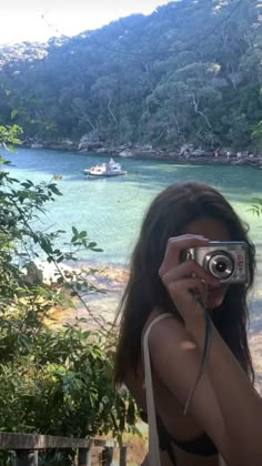 a woman taking a photo with her camera in front of a body of water and mountains