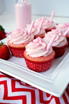 cupcakes with pink frosting and strawberries on a white plate next to a candle