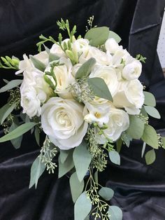 a bouquet of white roses and greenery on a black cloth