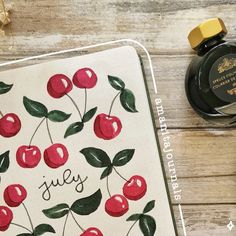 a notebook with cherries on it next to a bottle of ink