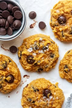 cookies with chocolate chips next to a cup of milk and cookie cutters on a white surface