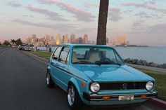 a blue car is parked on the side of the road near some water and palm trees