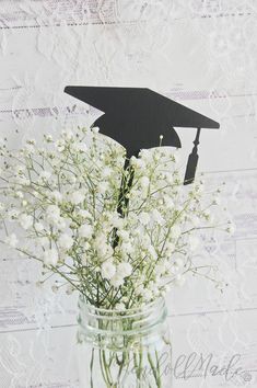 a mason jar filled with white flowers and a graduation cap cutout on the top