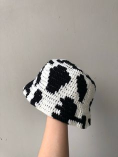 a hand is holding up a black and white knitted hat that looks like a cow pattern