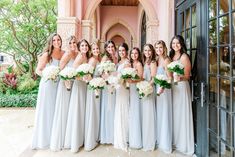 a group of women standing next to each other in front of a building holding bouquets