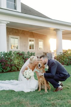 a bride and groom kissing their dog in front of a house with the sun behind them