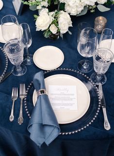 the table is set with silverware and white flowers