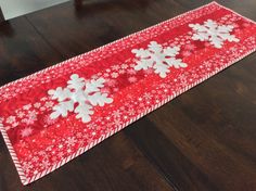 a red and white table runner with snowflakes on the edge, sitting on a wooden floor