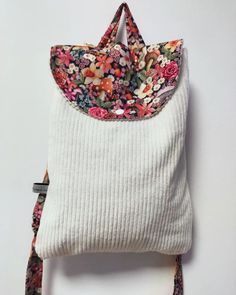 a white purse with flowers on it hanging from a hook in front of a wall