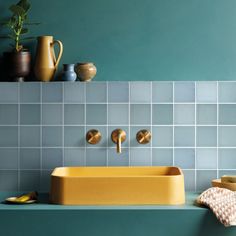 a yellow sink sitting on top of a counter next to a blue tiled bathroom wall