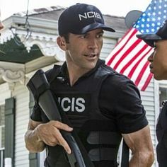 two police officers talking to each other in front of a house with an american flag