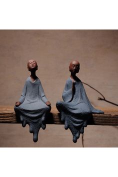 two small figurines sitting on top of a piece of wood with their eyes closed