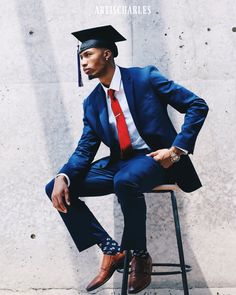 a man in a blue suit and red tie sitting on a chair wearing a graduation hat