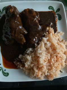 a white plate topped with rice and meat covered in gravy on top of a table