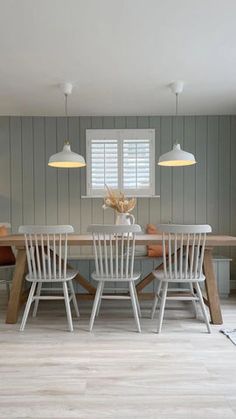 a dining room table with chairs and two lamps on each side, in front of a gray paneled wall