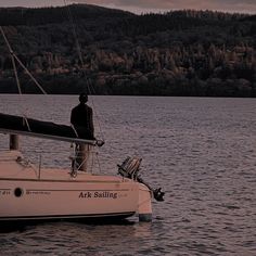 a man standing on top of a sailboat in the middle of a body of water