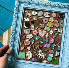 a person holding up a blue frame filled with different types of pins