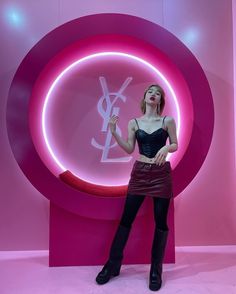 a woman standing in front of a pink wall with a lit up sign behind her