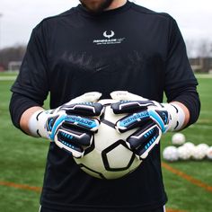 a man holding a soccer ball in his hands on a field with white and blue gloves