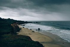 an ocean beach with waves coming in to shore and dark clouds overhead over the water