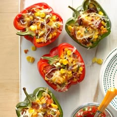 four peppers stuffed with corn and cheese are on a white tray next to a bowl