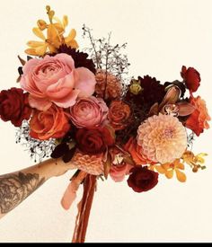 a bouquet of flowers is being held up by someone's hand with tattoos on their arm