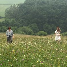 two people walking through a field with wildflowers